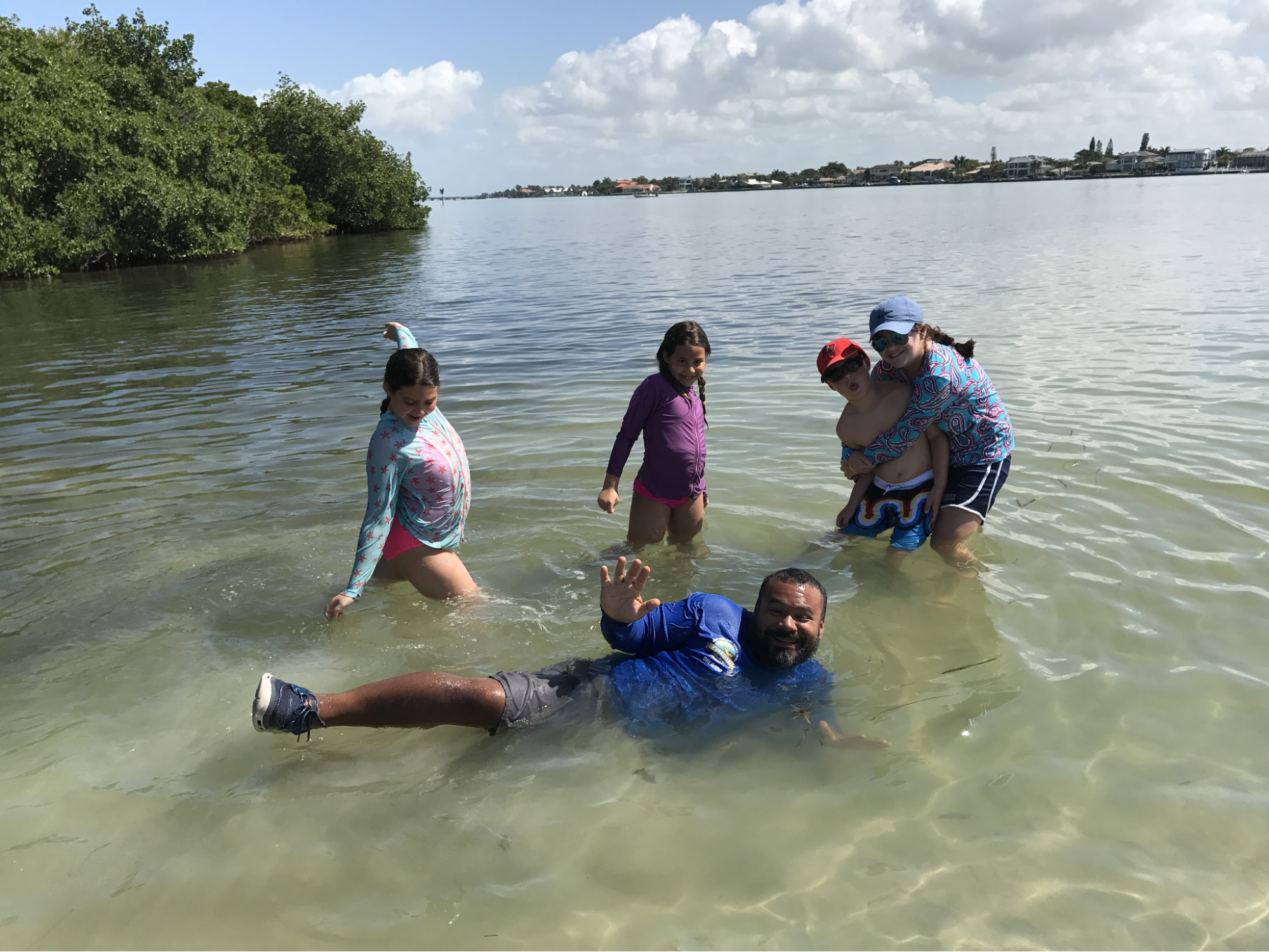 Four children smiling and playing together in the clear, shallow water of the Gulf Coast, enjoying a fun physical activity to burn off their summer energy.