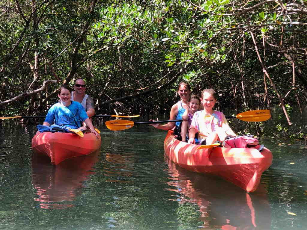 A family enjoying a guided eco-kayak tour through the Lido Key mangrove tunnels with Paradise Adventures.