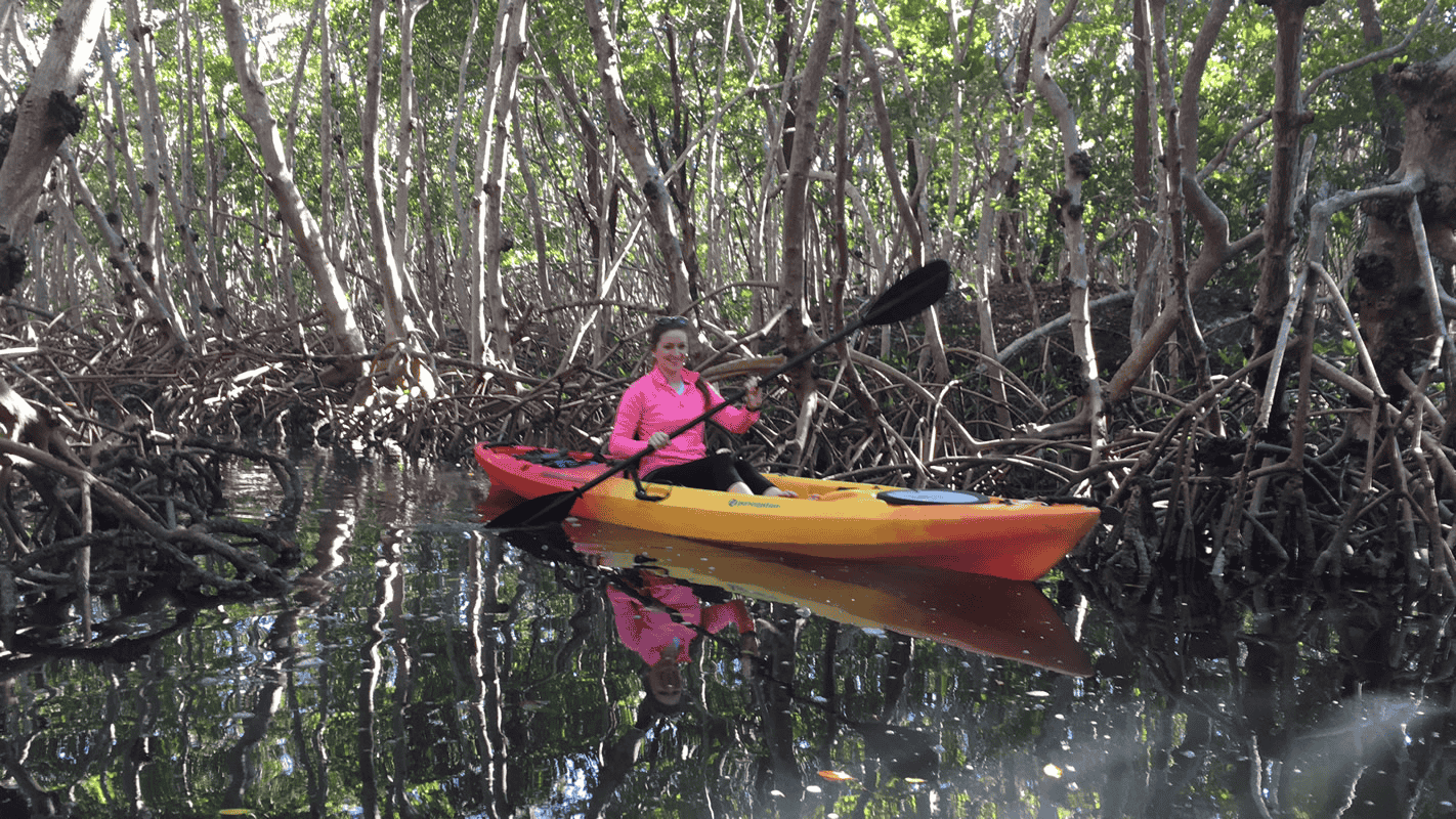 A woman smiling while paddling a kayak through a shaded red mangrove tunnel in Lido Key, Sarasota.